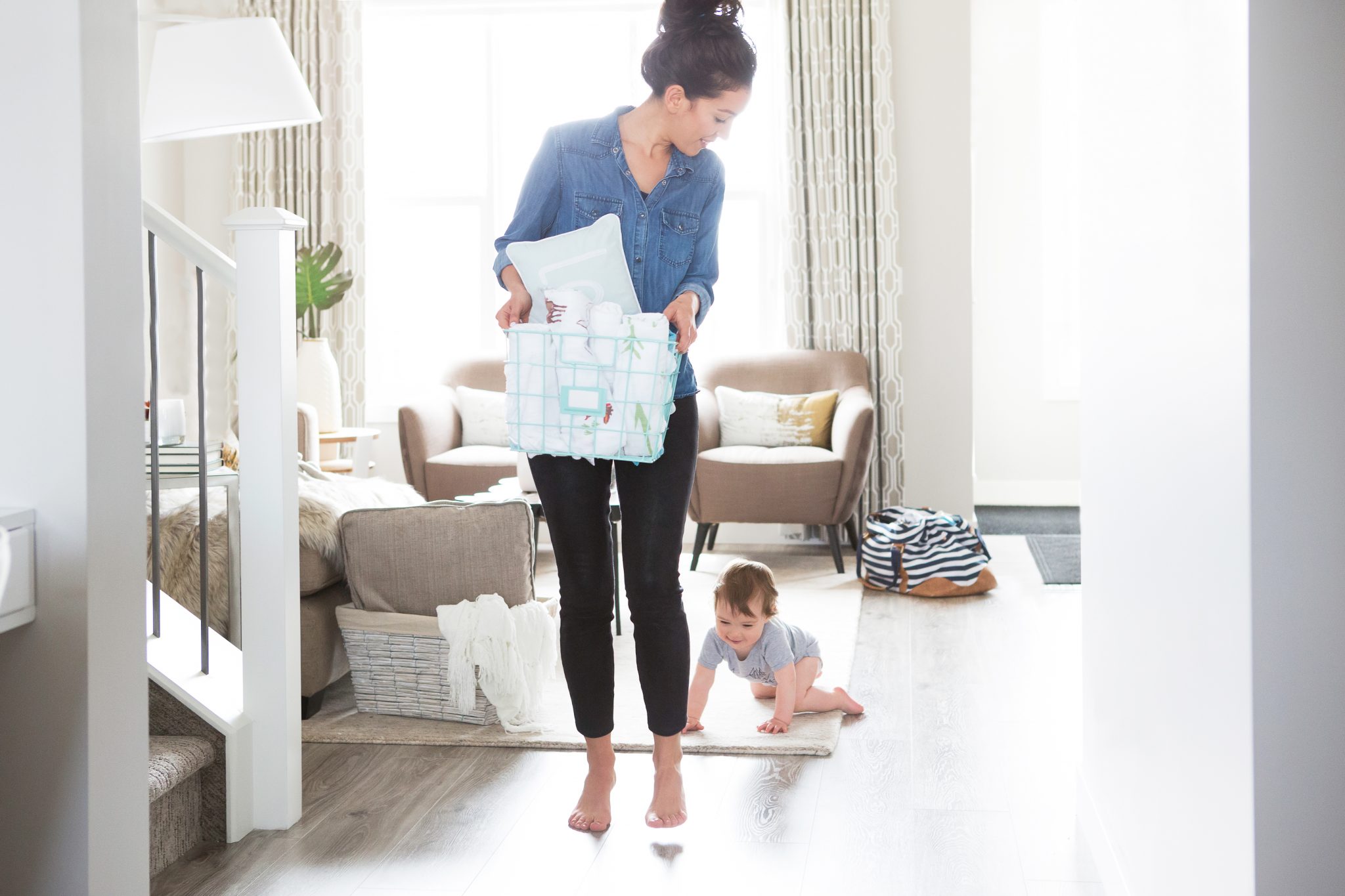 Stay at home mom doing laundry with crawling baby in tow. Many moms find that it's cheaper to be a stay at home mom, and it isn't just ditching daycare that saves you money.
